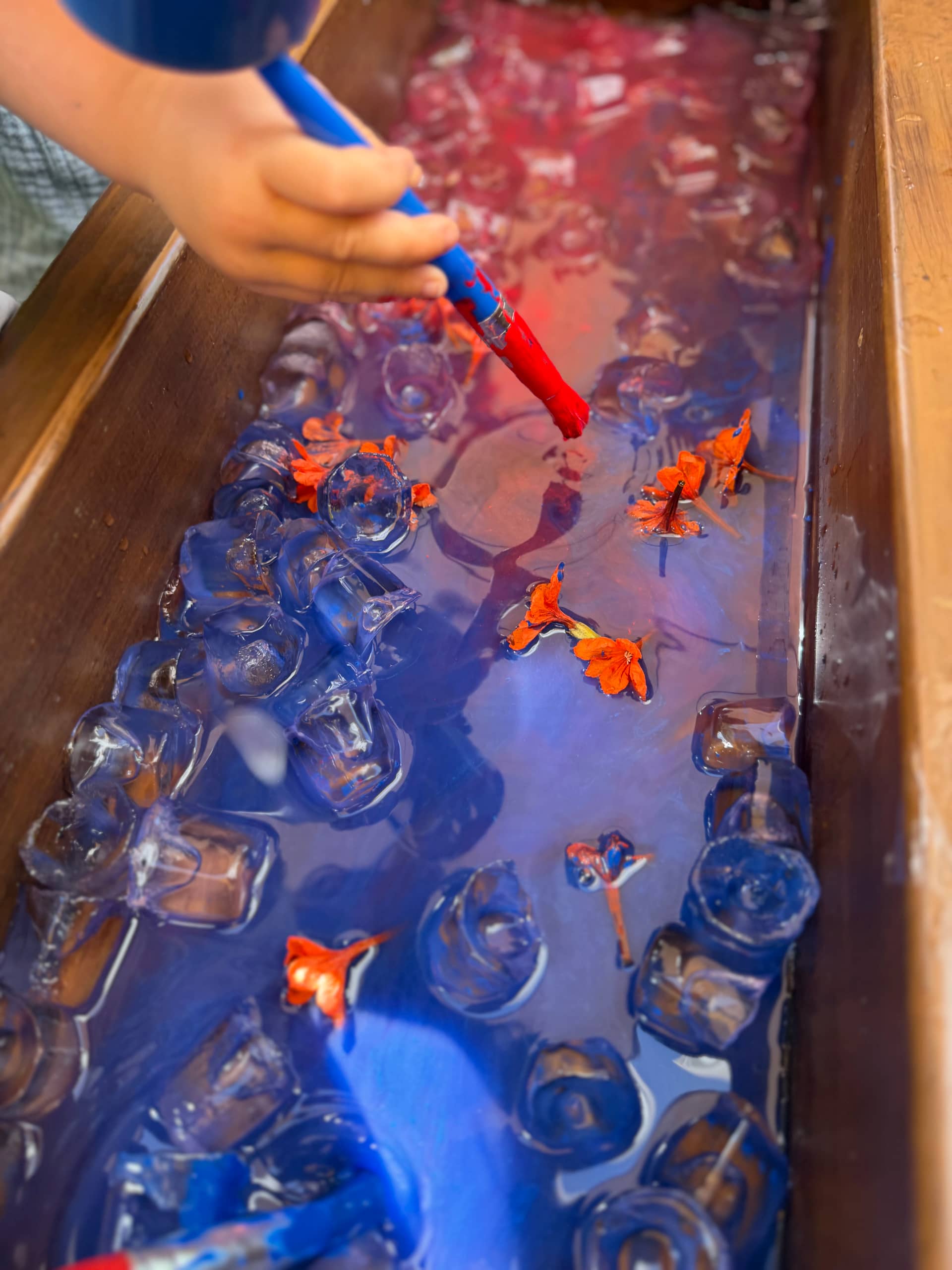 Child playing with ice, flowers and coloured water