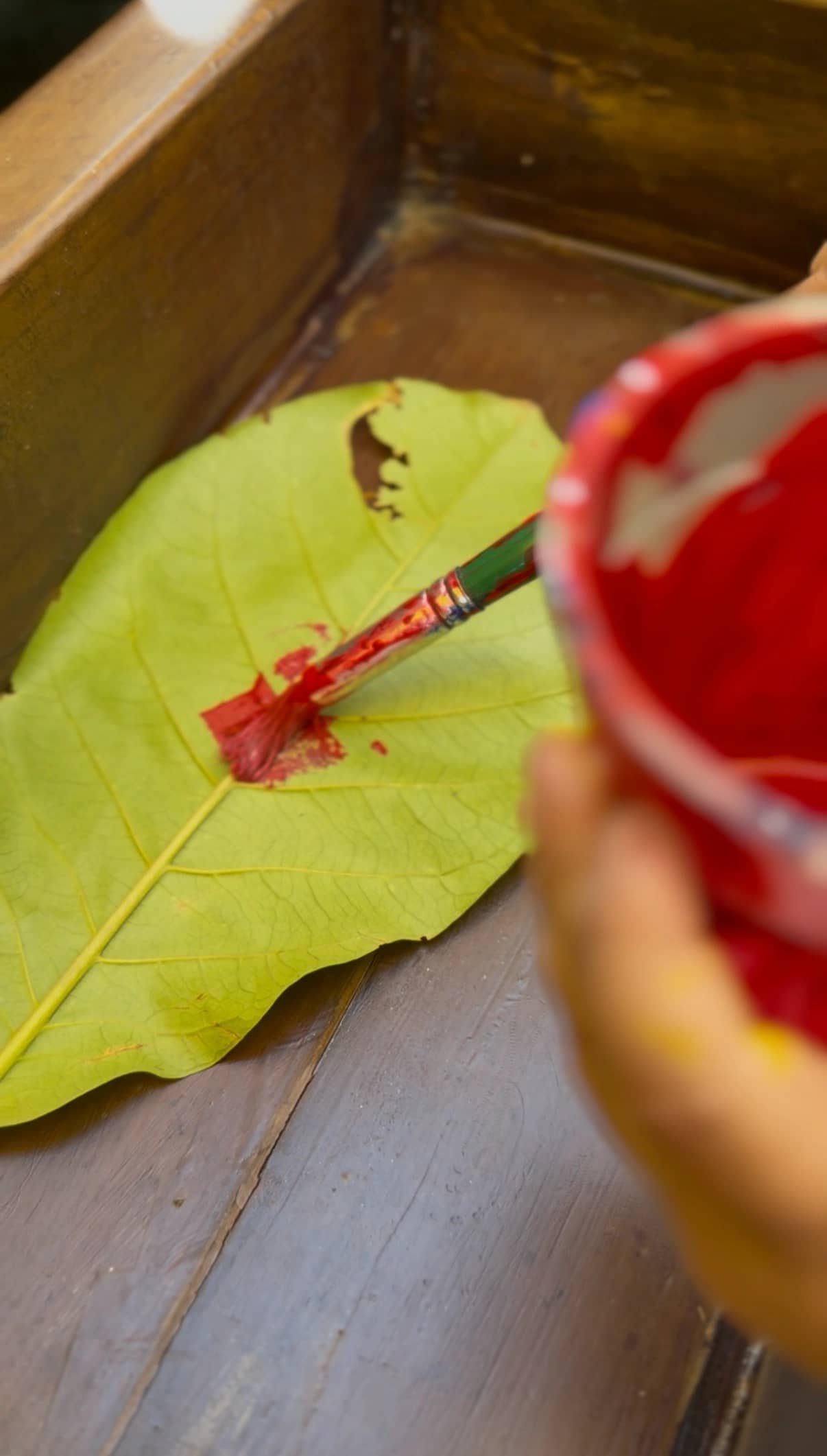 Child painting on a large leaf with red paint